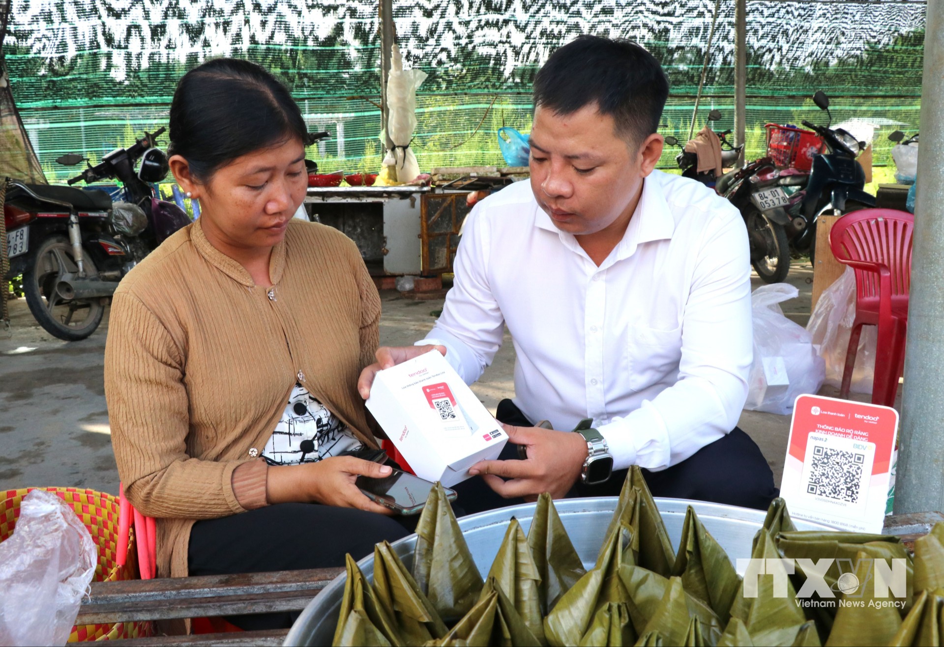 Đại diện Viettel trao và hướng dẫn tiểu thương chợ Cầu, xã Song Lộc, tỉnh Vĩnh Long, sử dụng bảng mã QR. (Ảnh: Thanh Hòa/TTXVN)
